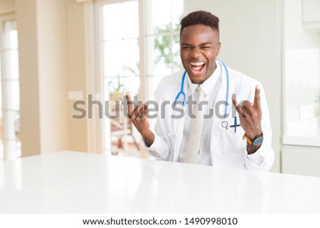 African american doctor man at the clinic shouting with crazy expression doing rock symbol with hands up. Music star. Heavy concept.