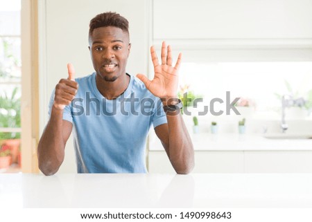 Handsome african american man wearing casual t-shirt at home showing and pointing up with fingers number six while smiling confident and happy.