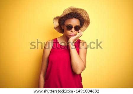 African american woman wearing summer hat and sunglasses over yellow isolated background thinking looking tired and bored with depression problems with crossed arms.
