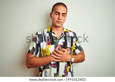 Young handsome man wearing summer shirt over white isolated background smiling with hands on chest with closed eyes and grateful gesture on face. Health concept.