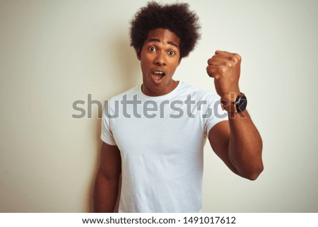 African american man with afro hair wearing t-shirt standing over isolated white background annoyed and frustrated shouting with anger, crazy and yelling with raised hand, anger concept