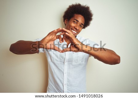 African american man with afro hair wearing shirt standing over isolated white background smiling in love showing heart symbol and shape with hands. Romantic concept.