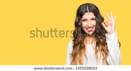 Young beautiful woman wearing white sweater smiling positive doing ok sign with hand and fingers. Successful expression.
