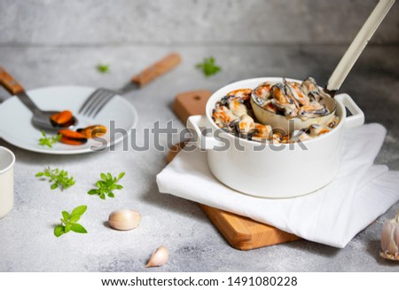Mussels in cream and white wine sauce. Served with garlic and herbs in a white pan with a ladle. Seafood gourmet dish. Light gray background. Front view