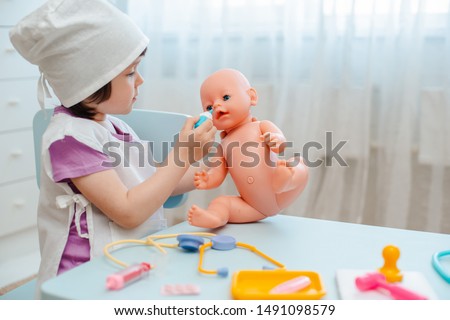 Little girl 3 years old preschooler playing doctor with doll. The child makes an injection toy. The concept of childhood vaccinations. Childhood in kindergarten role-playing educational games