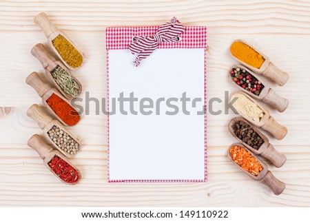 Recipe note book, spices in scoops on wood texture background