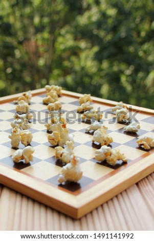 chessboard with popcorn instead of figures on a background of green summer garden, fast food concept