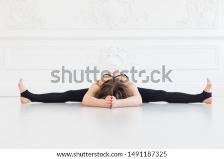 Blond woman in sport outfit doing splits on white bare floor