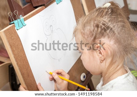 Little girl drawing a picture on easel in classroom