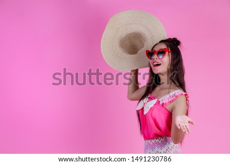 A beautiful woman wearing red glasses with a big hat on a pink background.