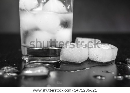 glass with ice on a black background. melting ice around splashing drops