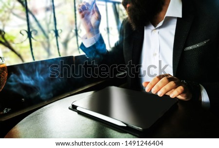 young adult bearded businessman with smart watch smoking cigar with blank pro tablet screen