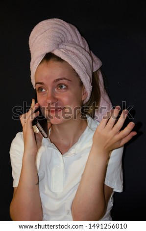 Girl with a towel on her head in a spa on a black background with cream in her hands talking on the phone
