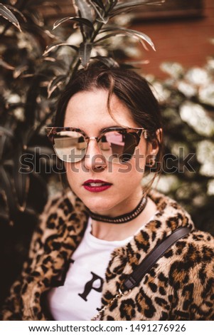 Close up stylish portrait of young serious woman wearing trendy leopartd print faux fur coat, fashion sunglasses, posing on grunge background