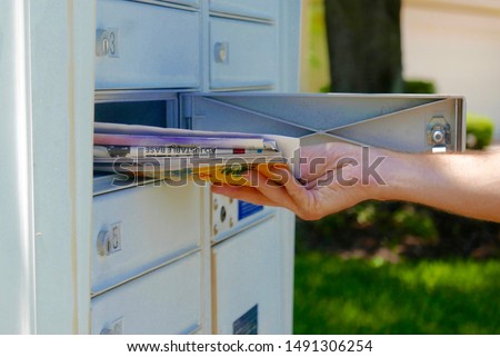 Person's hand pulling a pile of junk mail out of an outdoor community mailbox Royalty-Free Stock Photo #1491306254
