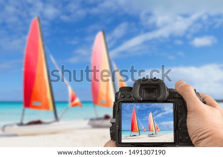 Travel phototography concept. Man's hands holding a DSLR camera taking picture of two catamarans