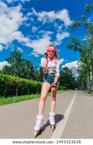 Portrait of an emotional beautiful young girl in a pink cap visor and protective gloves for rollerblades and skateboarding riding on rollerblades on the road.
