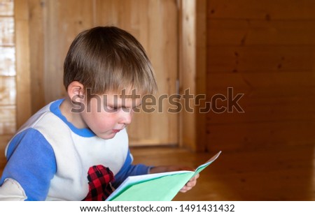 A boy first grader sits and looks in school notebook. Pensive sad schoolboy with a backpack and a notebook. First time to school. Child stress. White blond kid at home doing school homework.