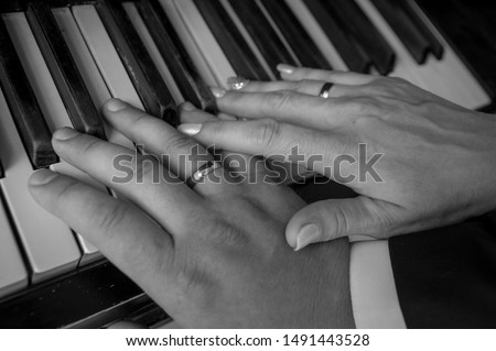 Hands of man and woman. Newlyweds are playing the piano. Hands of the newlyweds with wedding rings on the piano keys.