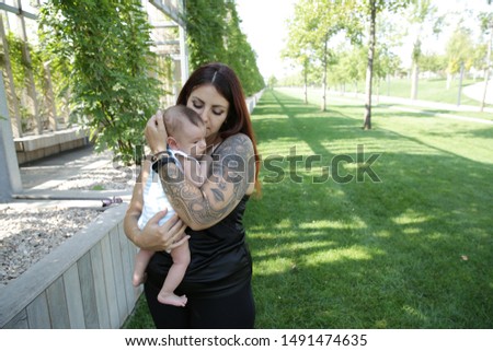 Portrait Happy young mother kisses her cute newborn baby. Happy family, motherhood, parenting, people and childcare concept. In the park.