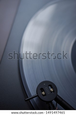 Modern round headshell with black cartridge on straight tonearm and transparent clear white vinyl record disc spinning on belt drive turntable