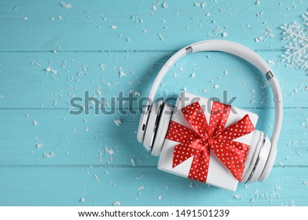 Modern headphones and gift box on blue wooden background, top view with space for text. Christmas music concept