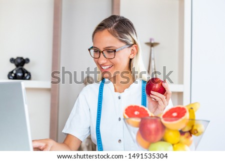 Doctor nutritionist writing case history in the office. Young woman dietitian prescribing recipe. Female nutritionist sitting at table with clipboard and healthy products on white background