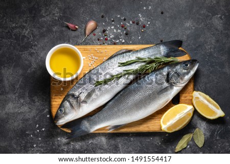 Fresh fish seabass and ingredients for cooking, lemon and rosemary. Dark background top view Royalty-Free Stock Photo #1491554417