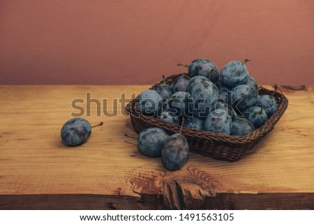 Close up beautiful fresh plums in basket  on a brown wooden table and red wall background.
