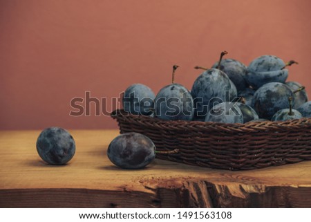 Close up beautiful fresh plums in basket  on a brown wooden table and red wall background.
