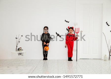 Two Asian child girls in halloween costumes with pumpkin, Funny kids in carnival costumes indoors