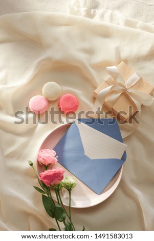 Envelope wih blank paper card on the light fabric background with lusianthus and gift box, top view