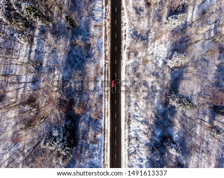 A road during winter. One Little red car giving contrast to the Image. 