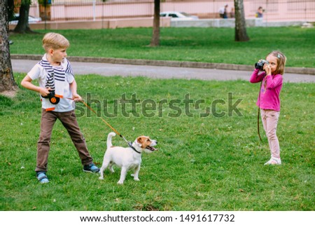 Little girl taking picture using vintage film camera. Cute little kid photographing her older brother with dog Jack Russell terrier posing on grass outdoor in park. Pet, love, friendship concept.