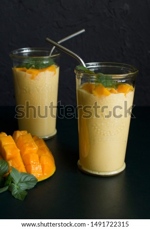 mango smoothie / mango lassi in vintage glass cups on a dark surface with metal straws. with mint leaves and a slice of ripe and juicy mango
