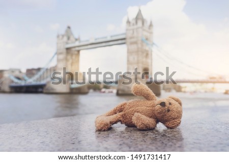 Teddy bear lying alone with blurry london tower bridge background, The forgotten bear sitting by the river, lost property, Lonely concept, Lost child, International missing child Royalty-Free Stock Photo #1491731417