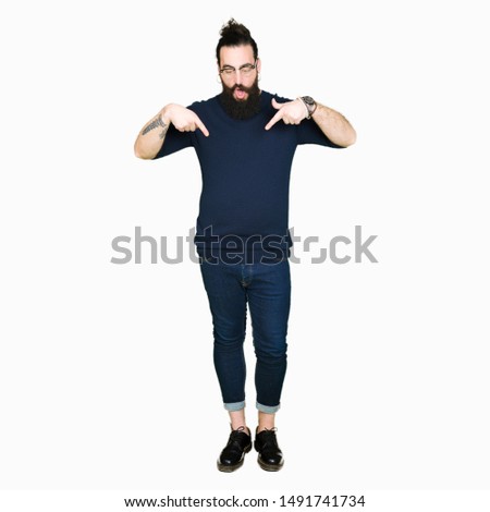 Young hipster man with long hair and beard wearing glasses Pointing down with fingers showing advertisement, surprised face and open mouth