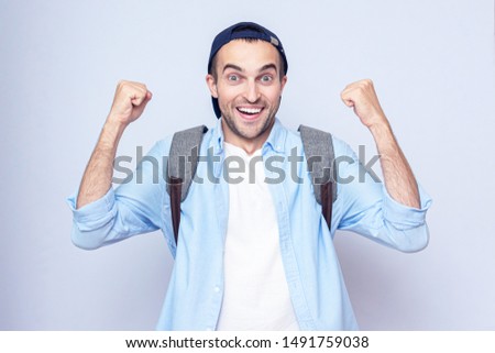 Young student guy with backpack screaming: Yes! Grey background, copy space