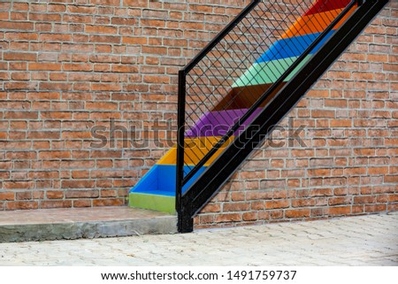 painted iron staircase in rainbow colors in front of a brick textured wall, front view