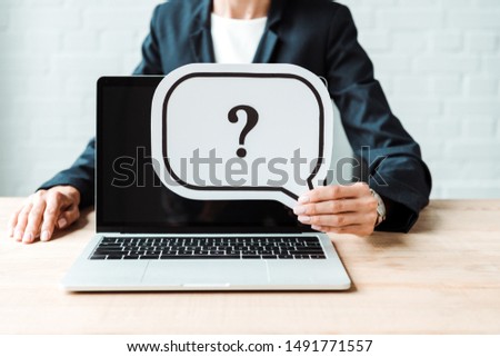 cropped view of woman holding speech bubble with question mark near laptop