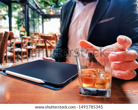 businessman holding whiskey in a glass with blank new pro tablet screen on the table