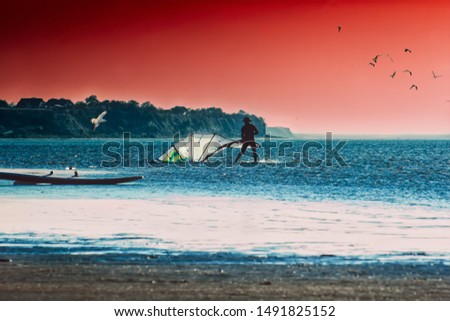 Silhouette of a surfer folds sail on the beach against the backdrop of the seascape and dramatic sunset