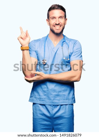 Handsome doctor man wearing medical uniform over isolated background with a big smile on face, pointing with hand and finger to the side looking at the camera.
