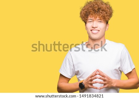 Young handsome man with afro hair wearing casual white t-shirt Hands together and fingers crossed smiling relaxed and cheerful. Success and optimistic