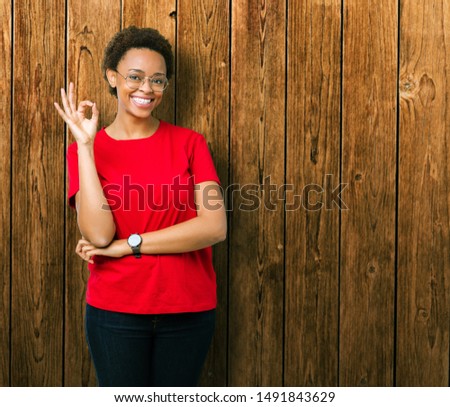 Beautiful young african american woman wearing glasses over isolated background smiling positive doing ok sign with hand and fingers. Successful expression.