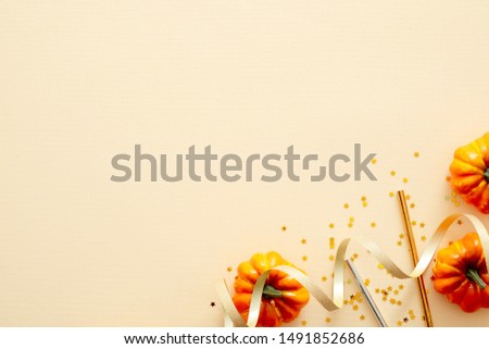 Halloween composition. Halloween decorations, pumpkins, confetti, gold ribbon on pastel beige background. Halloween party invitation card mockup. Flat lay, top view, copy space