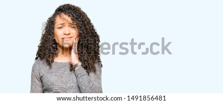 Young beautiful woman with curly hair wearing grey sweater touching mouth with hand with painful expression because of toothache or dental illness on teeth. Dentist concept.