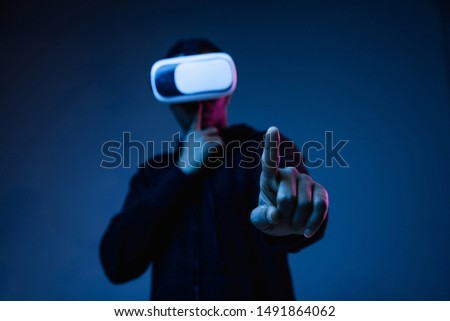 Young african-american man in VR-glasses in neon light on blue background. Male portrait. Concept of human emotions, facial expression, modern gadgets and technologies. Touching empty search bar.