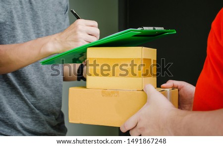 Postman delivering package of goods to home, Close up man hands signing to get his package from delivery man, Home delivery concept, Deliver packages to recipients quickly, complete products.