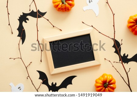 Happy Halloween concept. Halloween decorations, picture frame, pumpkins, bats, ghosts on pastel beige background. Halloween party greeting card mockup with copy space. Flat lay, top view.